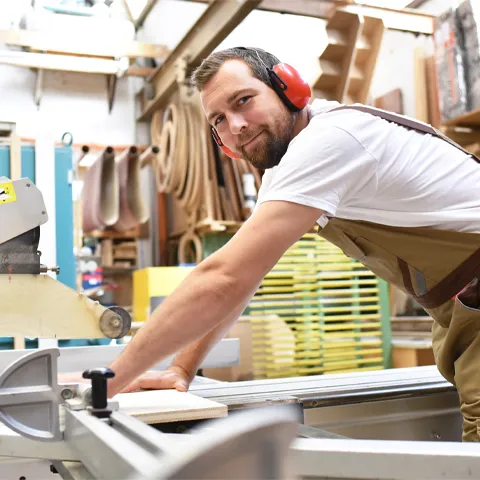 friendly carpenter with ear protectors and working clothes working on a saw in the workshop